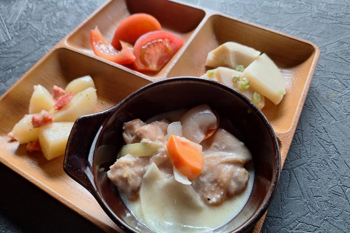 仕切りのある木のお皿に、シチューと副菜が盛られた昼食
